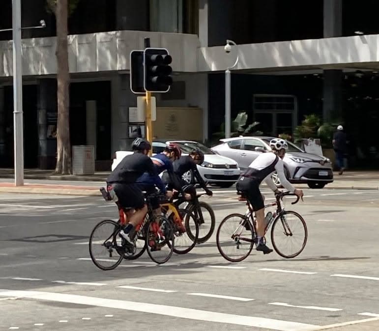 A group of cyclists riding through a city intersection alongside cars