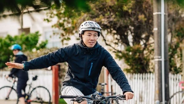 A cyclist giving a clear hand signal while riding with the flow of traffic on a residential street